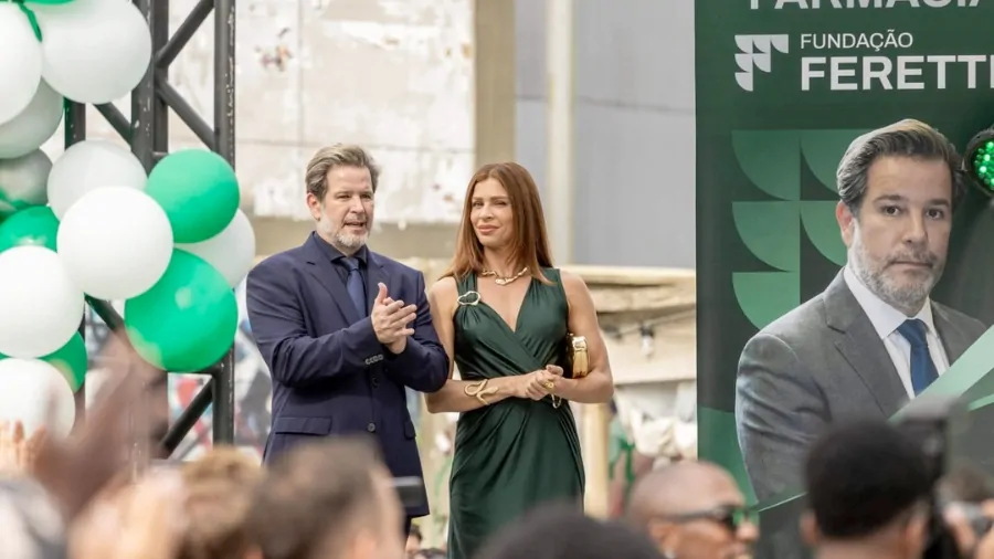 Ferette e Arminda aparecem juntos em evento público da Fundação Ferette, bem vestidos e em posição de destaque diante de plateia, em cena da novela Três Graças que retrata o auge de poder do casal antes da derrocada.